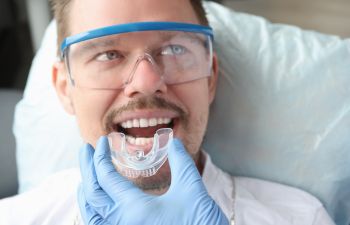 A dentist trying custom dental nightguards on male patient's teeth.