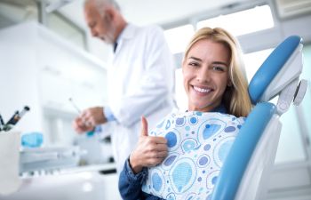 Smiling satisfied woman sitting in a dental chair after tooth treatment and showing her thumb up.