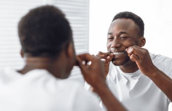 Afrom-American man flossing his teeth in front of the bathroom mirror.