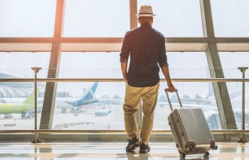 A man with a travel suitcase wearing a summer hat waiting for his flight at an airport.