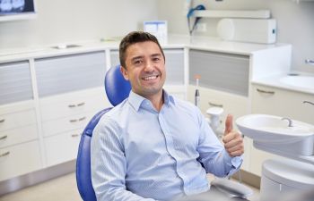 a satisfied man sitting in a dental chair and showing his thumb up