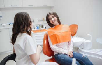 A dentist discussing the treatment with a young woman sitting in a dental chair.