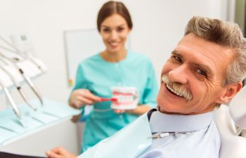 a senior man in a dental chair and a hygienist with a dental model showing how to clean teeth