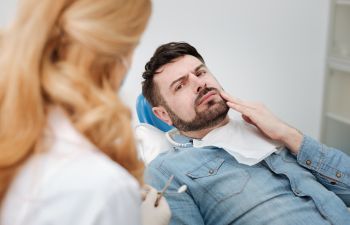 A concerned man in a dental chair explaining the issue to a dentist