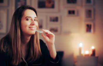 Young woman sitting in a bed and putting teeth nightguard before going to sleep.